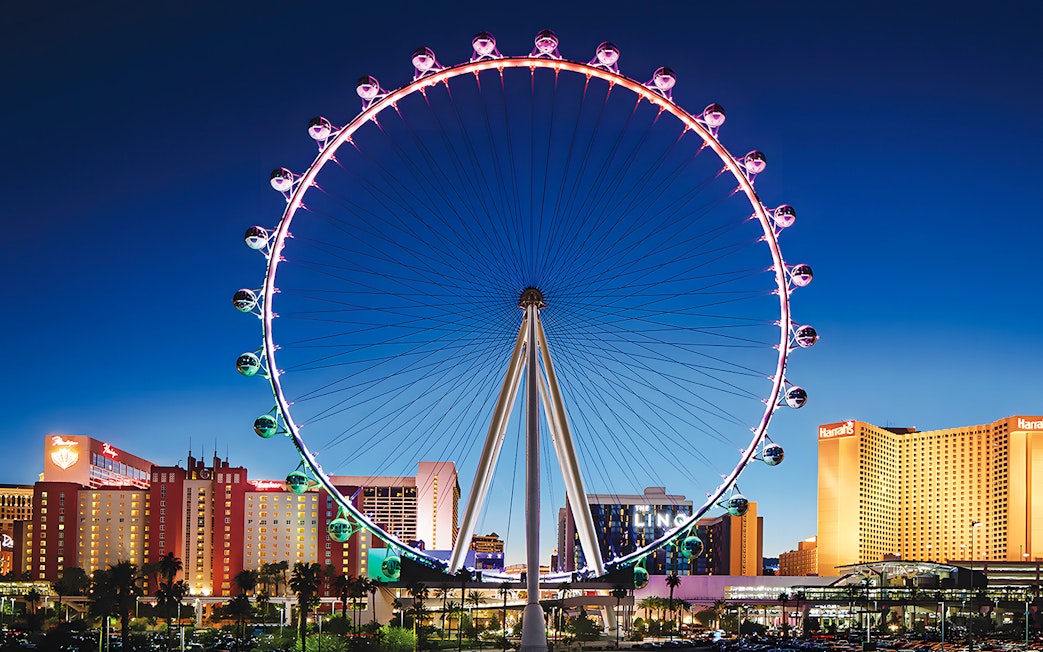 High Roller Wheel illuminated at night, Las Vegas skyline in background.
