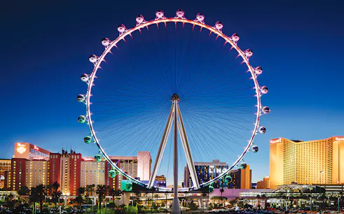 High Roller Wheel illuminated at night, Las Vegas skyline in background.