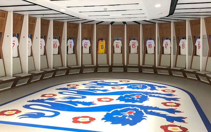 Wembley Stadium dressing room with England football jerseys displayed.