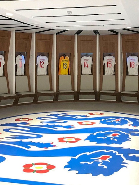 Wembley Stadium dressing room with England football jerseys displayed.