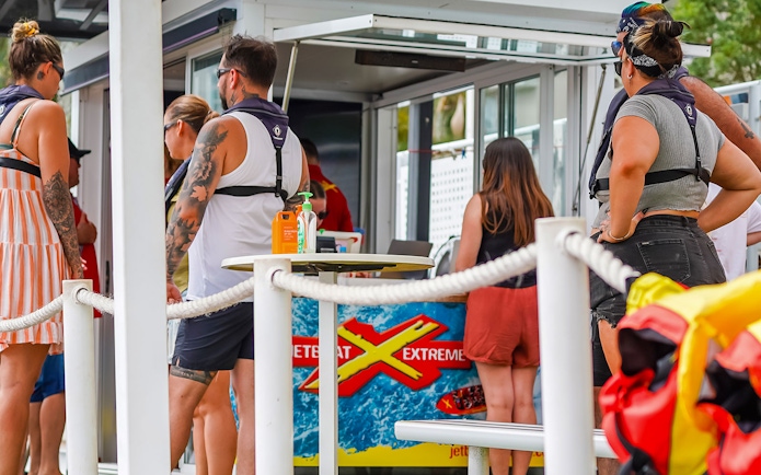 People preparing for the Ultimate Jet Boat Ride at a waterfront kiosk.