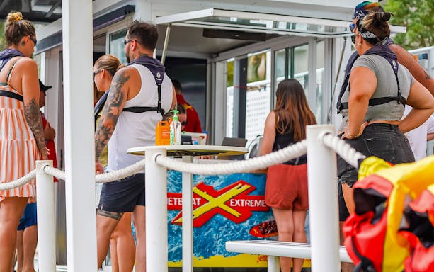 People preparing for the Ultimate Jet Boat Ride at a waterfront kiosk.