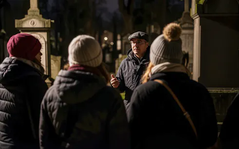 Tour guide leading a haunted cemetery bus tour at night.