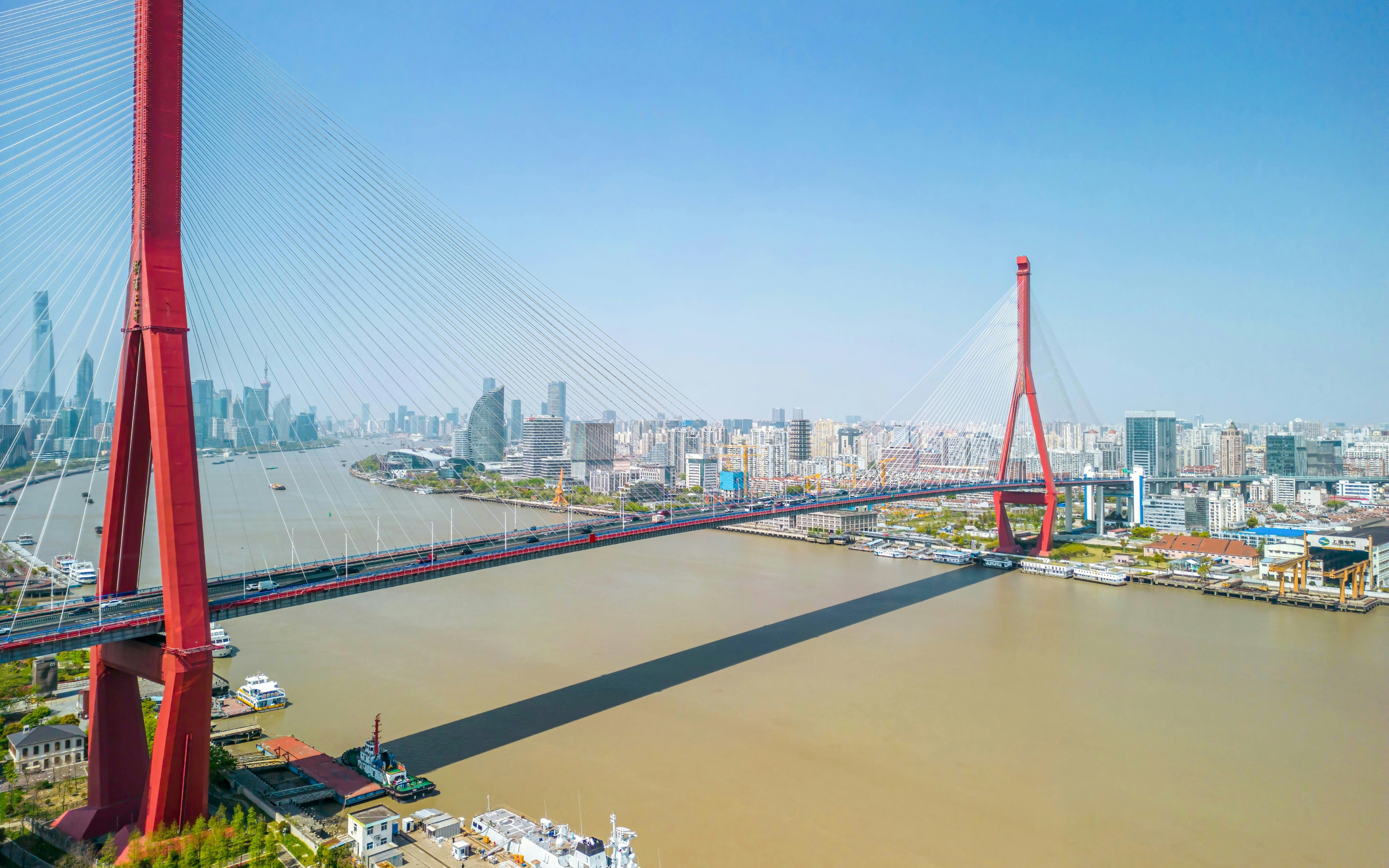 Drone view of Yangpu Bridge spanning Huangpu River, Shanghai, China, with city skyline in background.