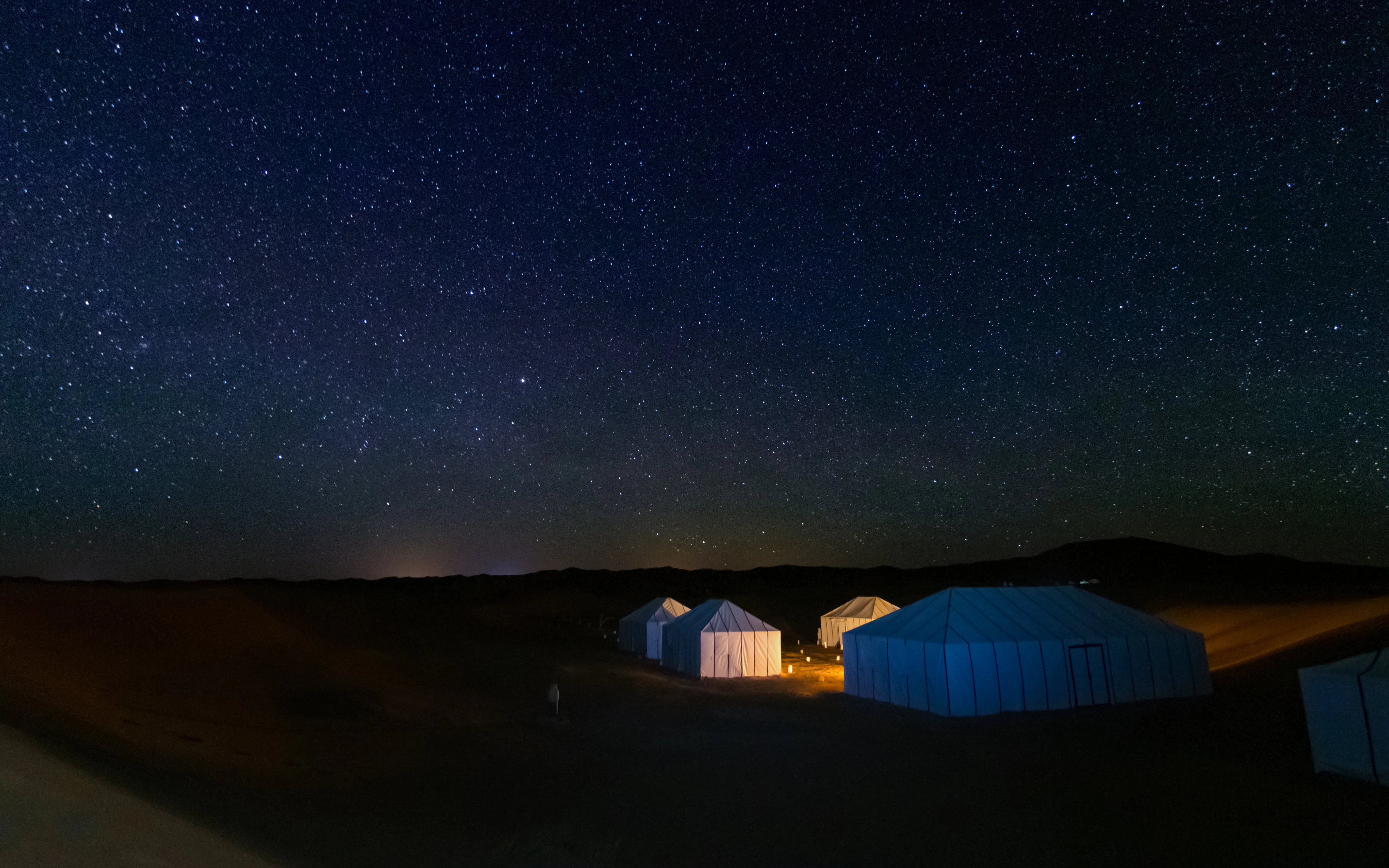 Illuminated tents in Erg Chebbi desert, Merzouga, under starry sky, Morocco.