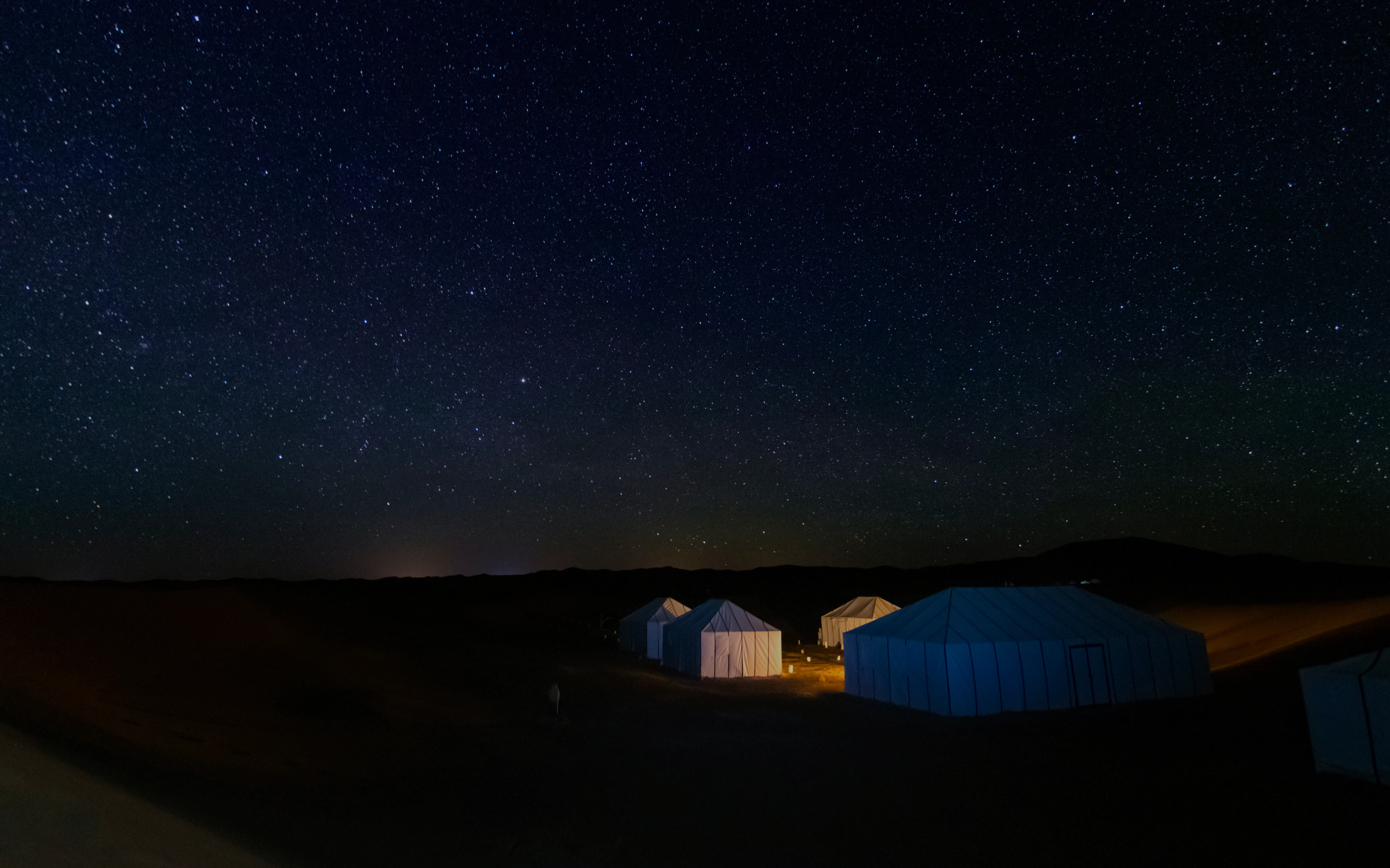 Illuminated tents in Erg Chebbi desert, Merzouga, under starry sky, Morocco.