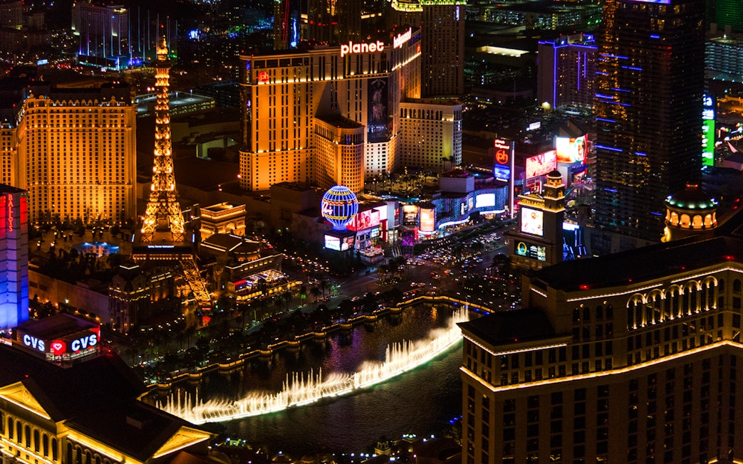 Aerial view of the illuminated Las Vegas Strip at night featuring the Eiffel Tower replica and Bellagio fountains.