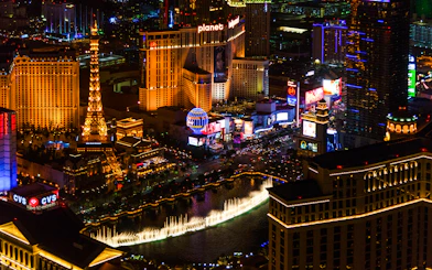 Aerial view of the illuminated Las Vegas Strip at night featuring the Eiffel Tower replica and Bellagio fountains.