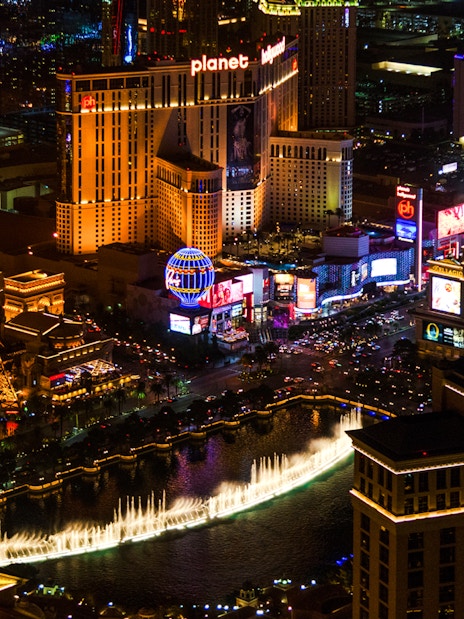 Aerial view of the illuminated Las Vegas Strip at night featuring the Eiffel Tower replica and Bellagio fountains.