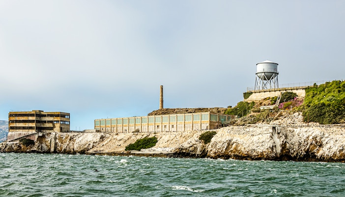 New Industries Building and water tower on Alcatraz Island, viewed from the water under a cloudy sky.