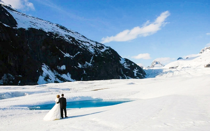 Couple standing on a glacier during Juneau helicopter tour with dog sledding.