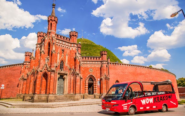 Red hop-on hop-off bus in front of Kraków's Kościuszko Mound and neo-Gothic chapel.