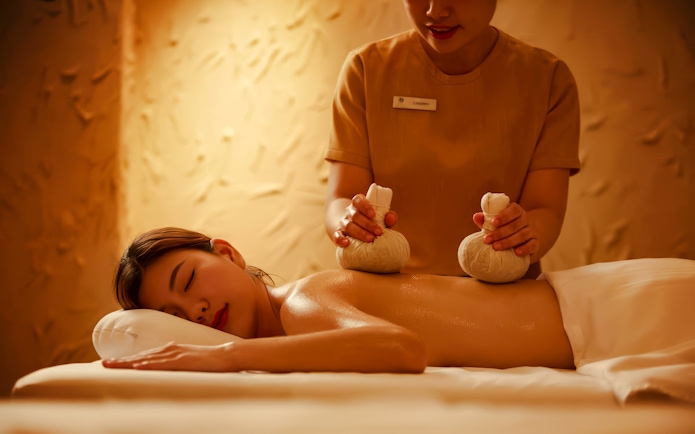 Massage therapist applying herbal compress on client's back.