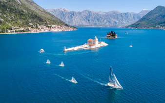 Aerial view of Our Lady of the Rocks with speedboat and sailboats in Kotor Bay, Montenegro.