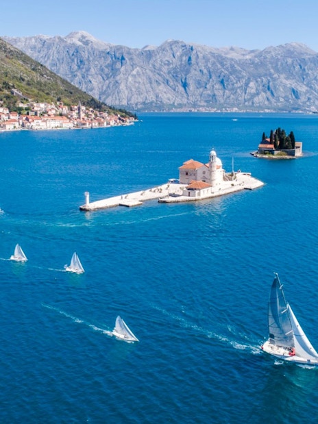 Aerial view of Our Lady of the Rocks with speedboat and sailboats in Kotor Bay, Montenegro.