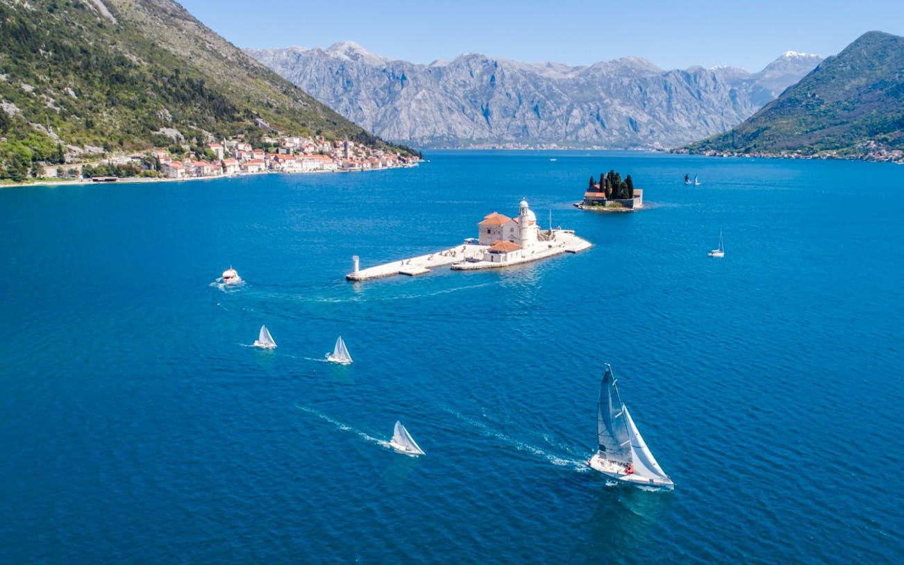 Aerial view of Our Lady of the Rocks with speedboat and sailboats in Kotor Bay, Montenegro.