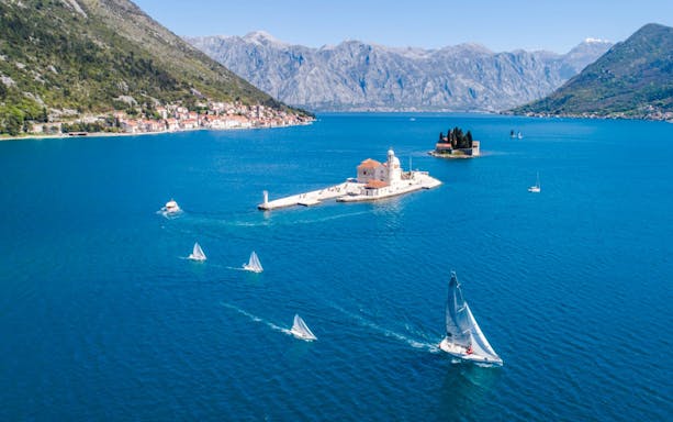 Aerial view of Our Lady of the Rocks with speedboat and sailboats in Kotor Bay, Montenegro.