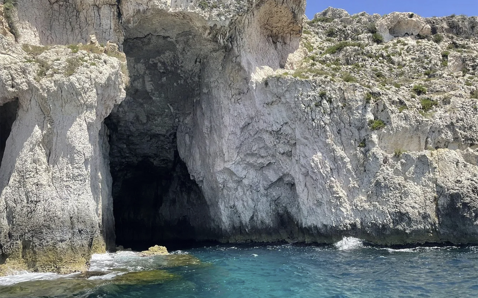 Boat entering a grotto at Ortigia Island, Sicily, showcasing natural rock formations.
