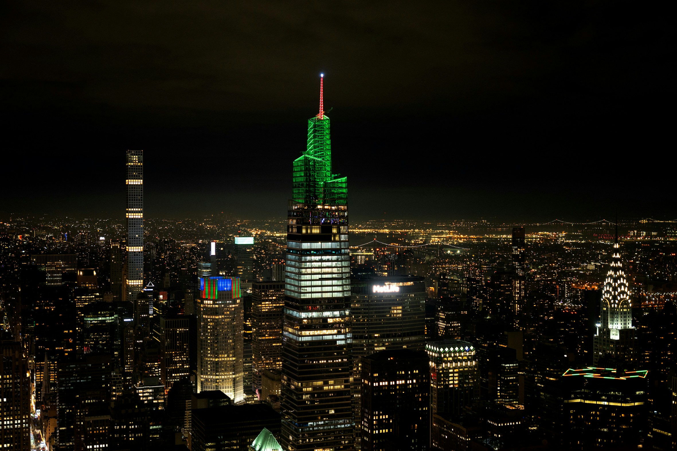Summit One Vanderbilt illuminated at night with Christmas lights, New York City skyline in background.