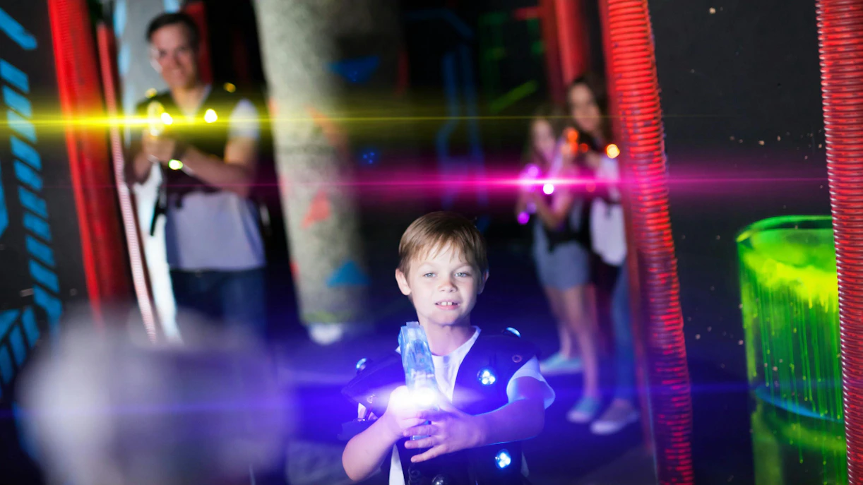 Child playing laser tag in a neon-lit arena with glowing vests and laser beams.