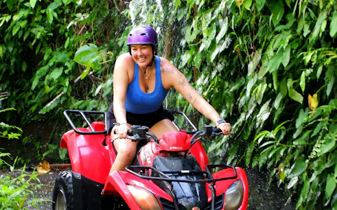 Tourist riding a red quad bike through lush greenery in Bali.