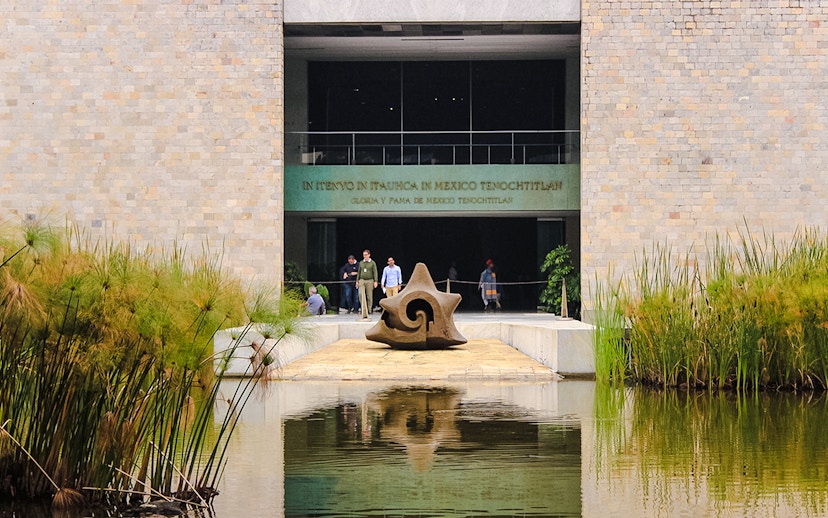 Entrance of the Anthropology Museum in Mexico City with a stone sculpture and reflecting pool.