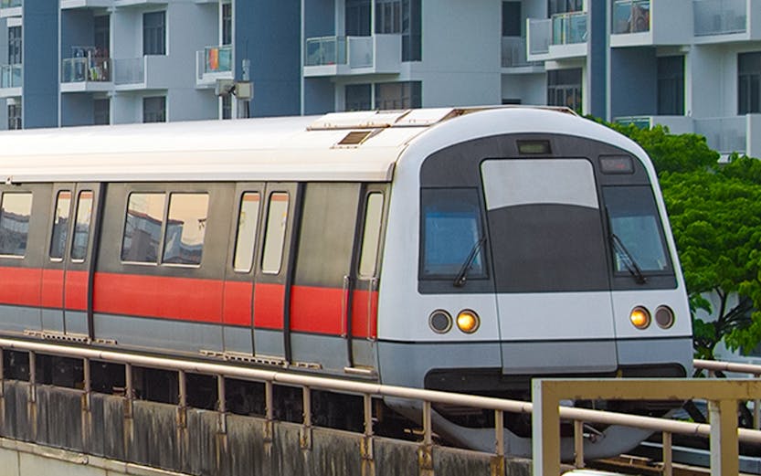 Metro train on elevated track with buildings in Singapore.