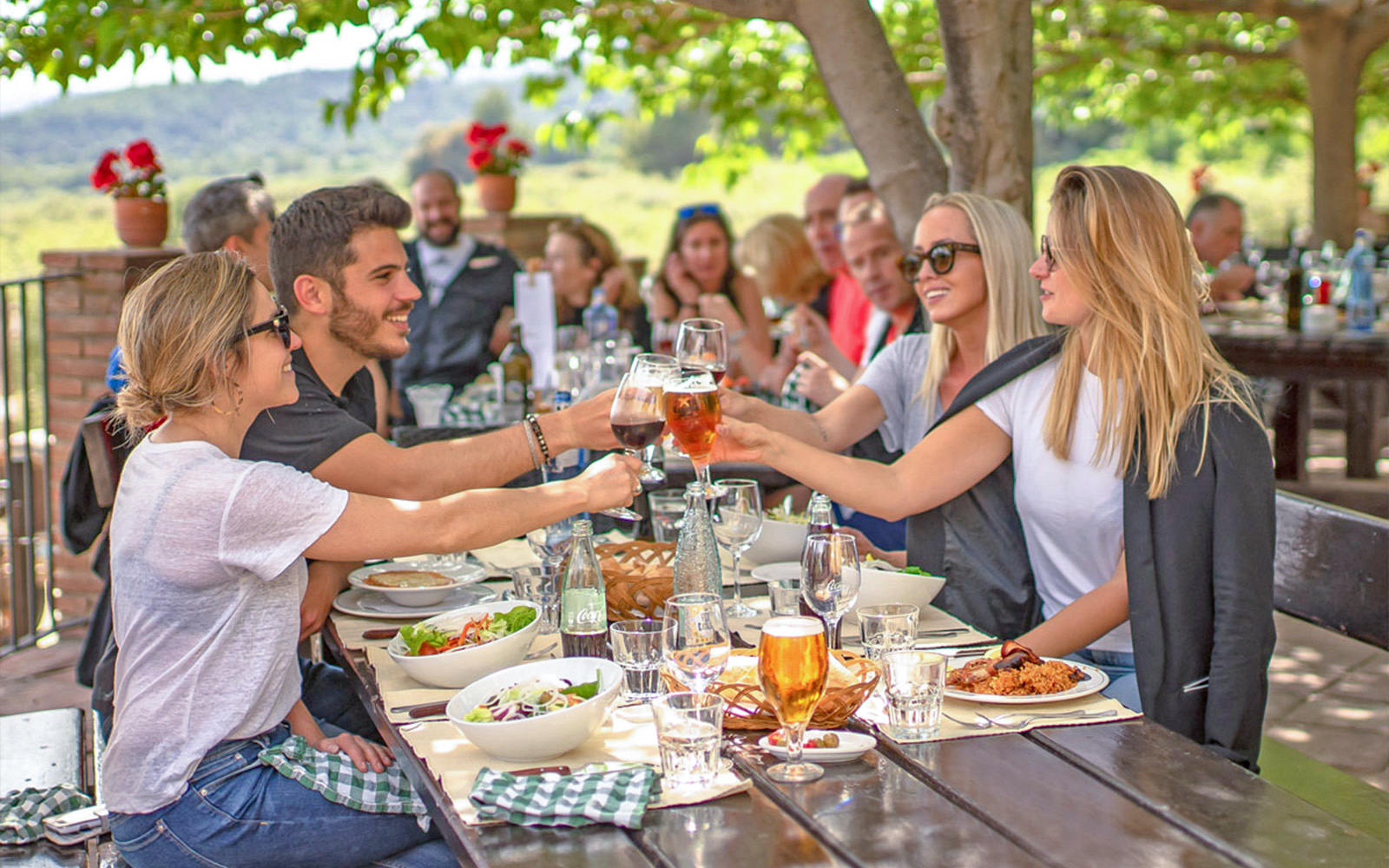 Lunch gathering during Montserrat monastery tour with people toasting at an outdoor table.