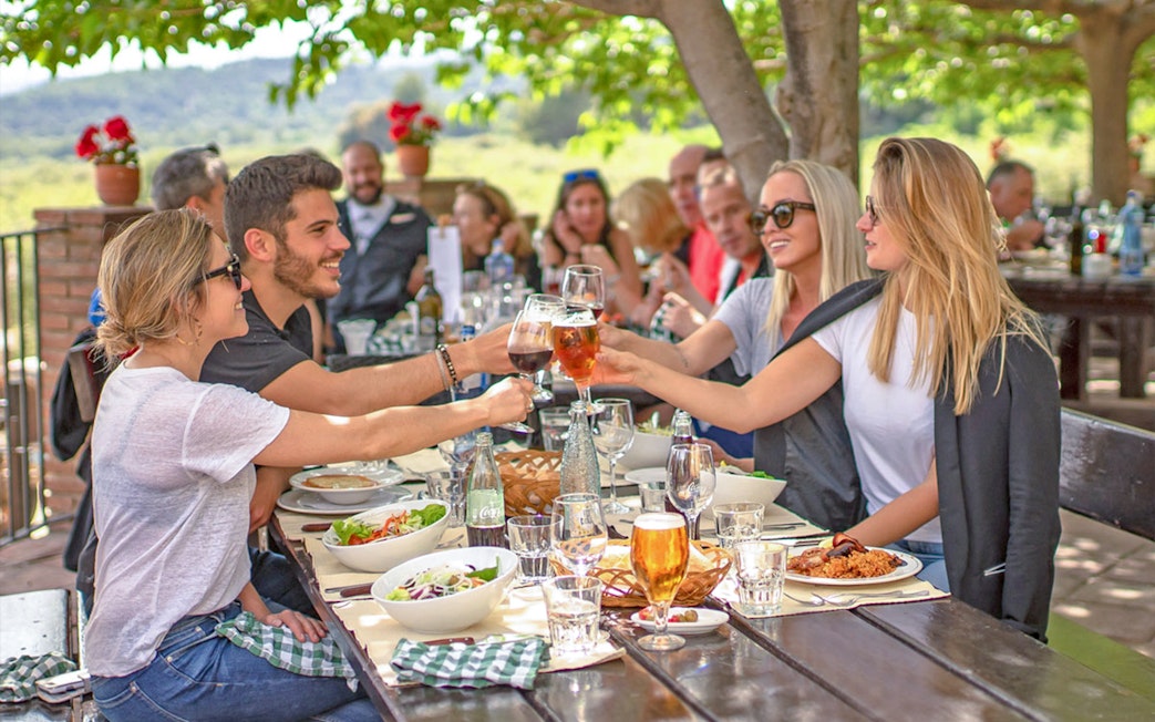 Lunch gathering during Montserrat monastery tour with people toasting at an outdoor table.