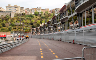 Monaco Formula 1 pit lane with grandstands and hillside buildings in the background.
