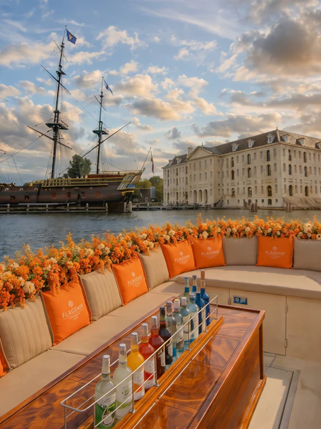 Luxury boat with drinks on Amsterdam canal near historic ship and building.