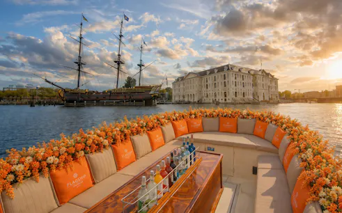 Luxury boat with drinks on Amsterdam canal near historic ship and building.