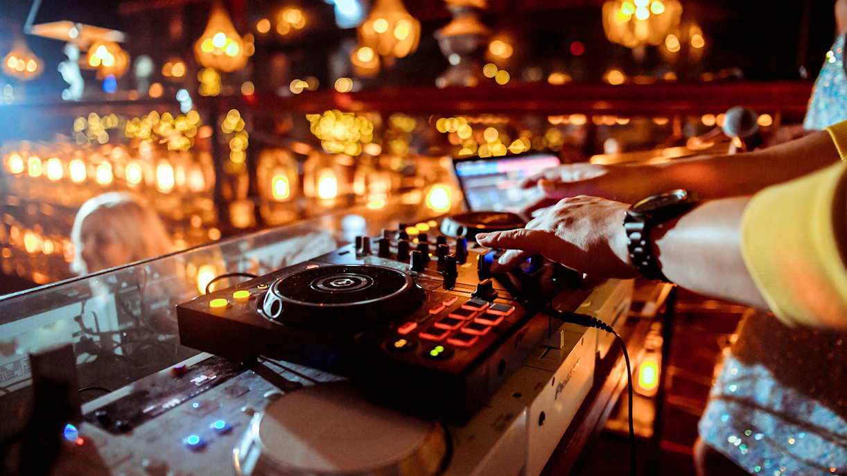DJ mixing music at a lively event with colorful lights and a vibrant atmosphere.