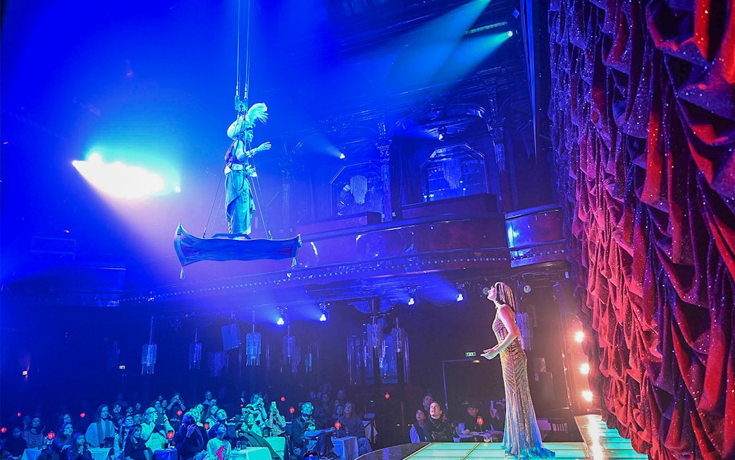 Performer on stage with aerial act at Paris cabaret show, audience watching.