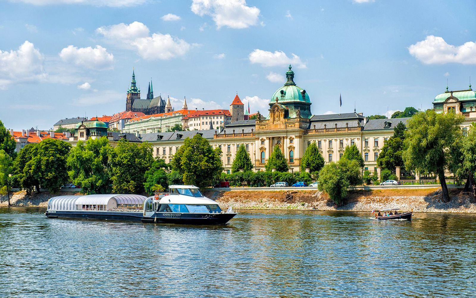Prague river cruise boat on Vltava River with Charles Bridge in the background.