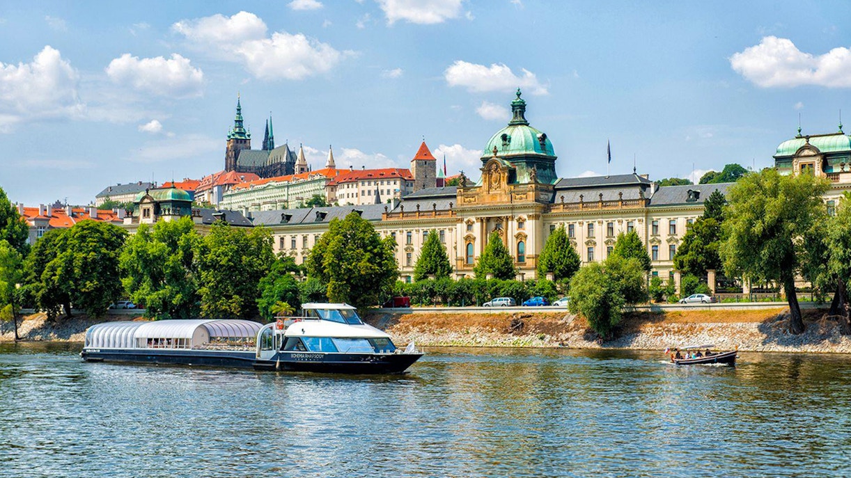 Prague river cruise boat on Vltava River with Charles Bridge in the background.