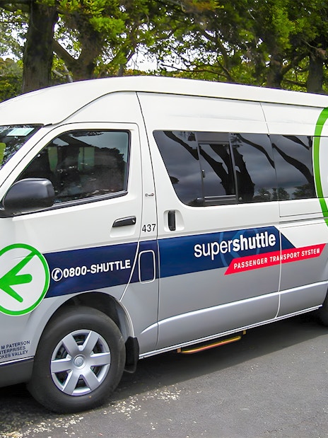 Super Shuttle van parked in a green park setting for airport transfers.