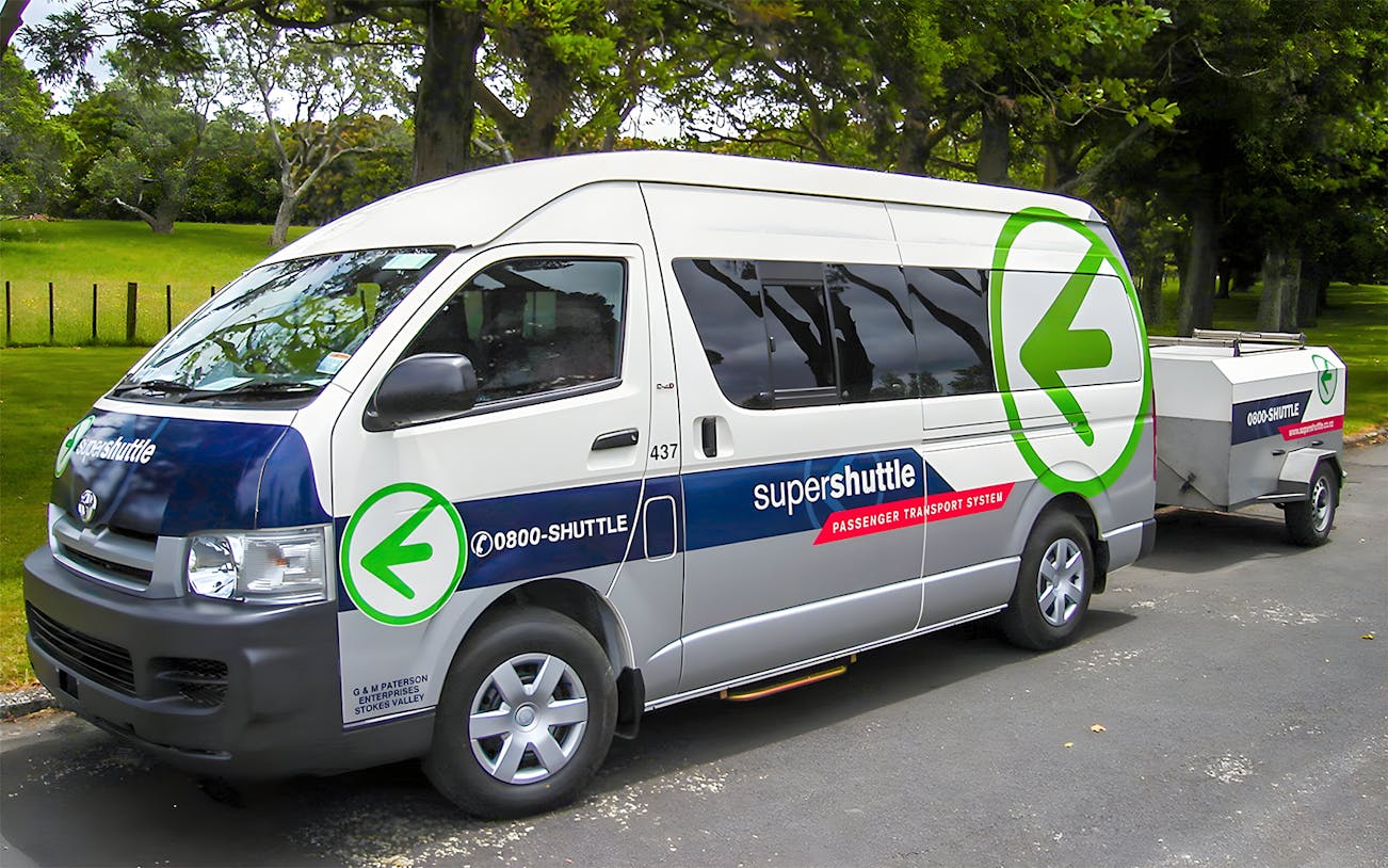 Super Shuttle van parked in a green park setting for airport transfers.