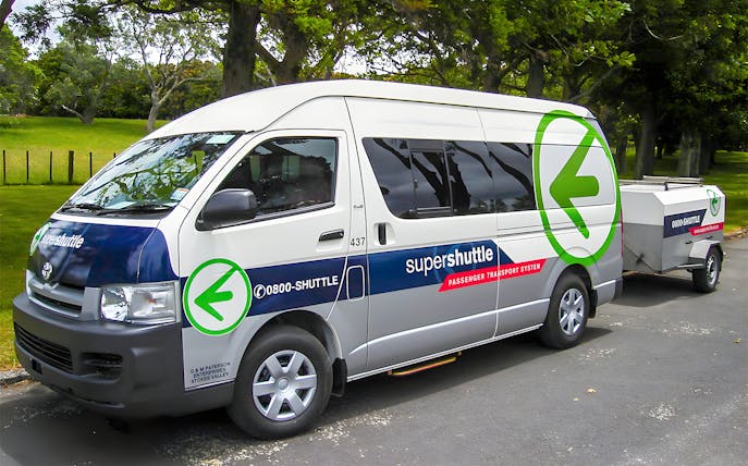 Super Shuttle van parked in a green park setting for airport transfers.