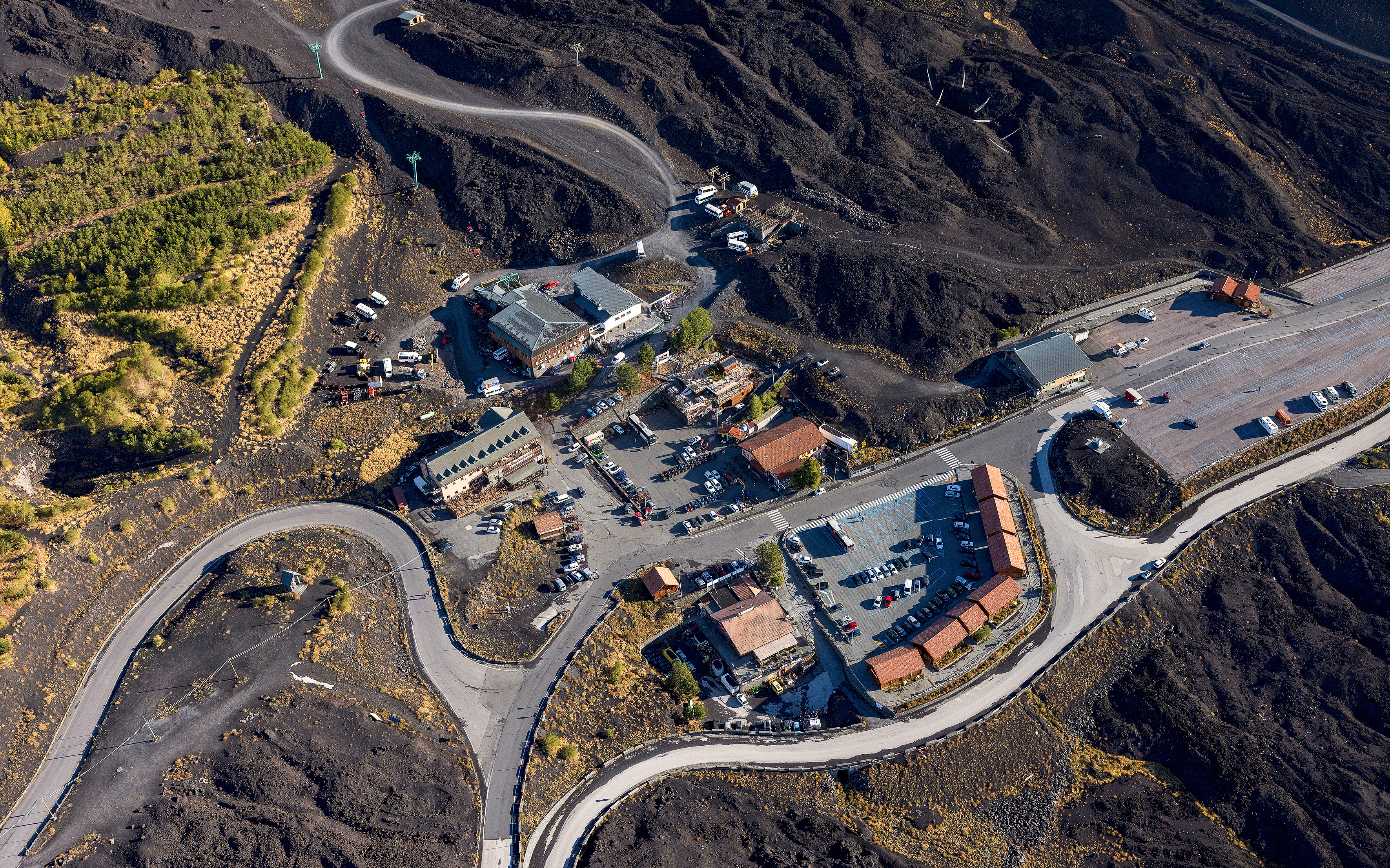 Aerial view of Rifugio Sapienza at Mount Etna entrance with winding roads and parking area.