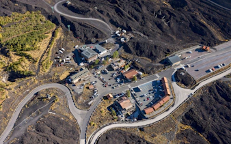 Aerial view of Rifugio Sapienza at Mount Etna entrance with winding roads and parking area.