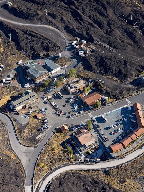 Aerial view of Rifugio Sapienza at Mount Etna entrance with winding roads and parking area.