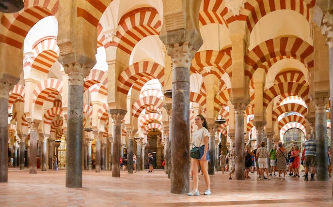 Women walking inside the Mosque-Cathedral of Cordoba, Spain, with iconic arches.