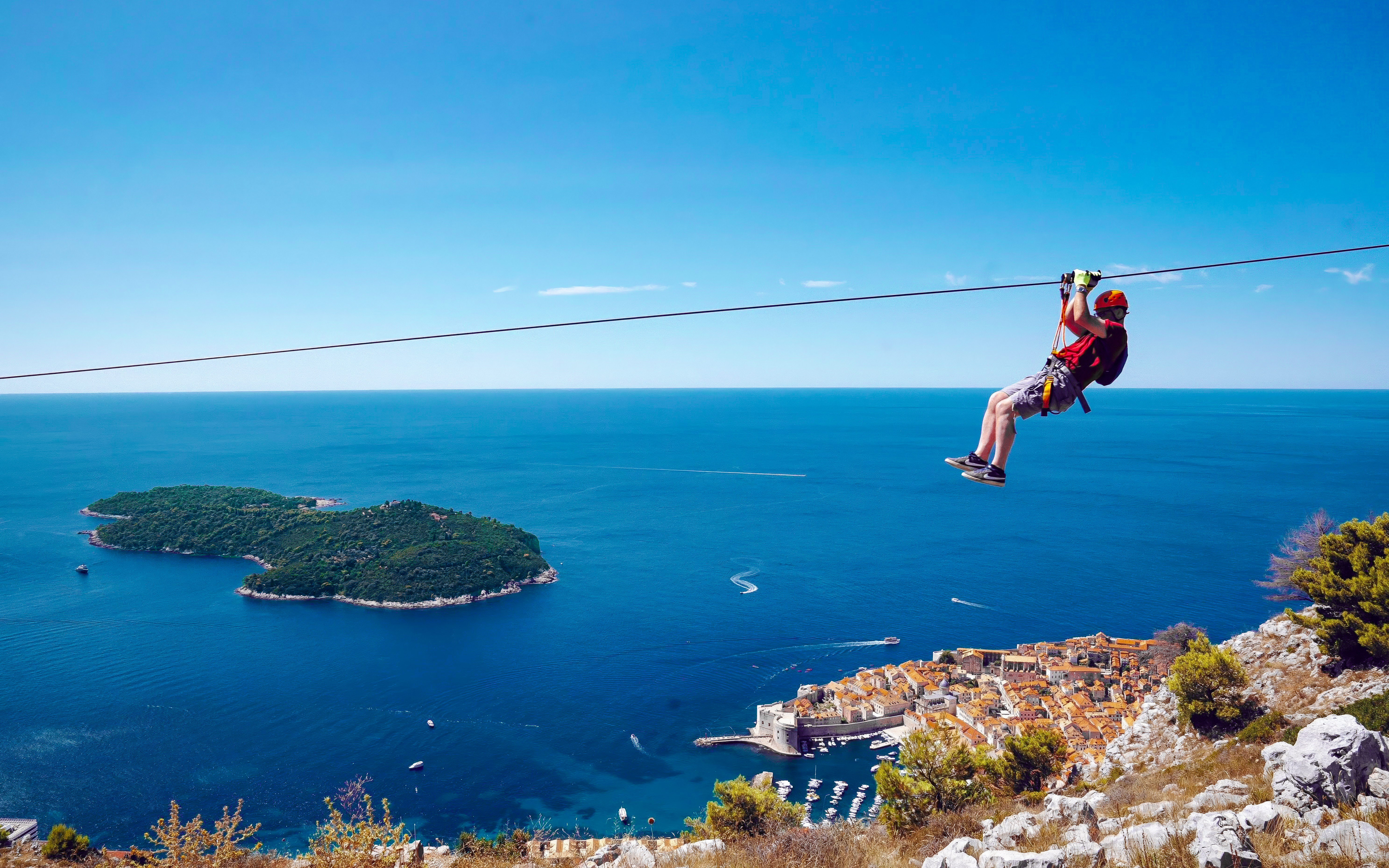 Zip lining over Pasjača Beach, Croatia with view of Adriatic Sea and coastal town.