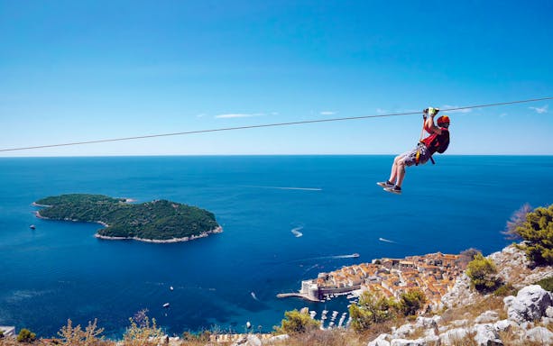 Zip lining over Pasjača Beach, Croatia with view of Adriatic Sea and coastal town.