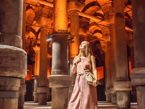 Visitor exploring the illuminated columns of the Basilica Cistern in Istanbul.
