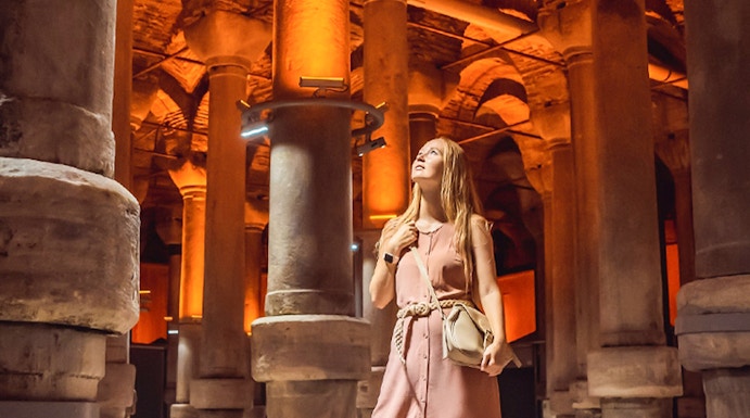 Visitor exploring the illuminated columns of the Basilica Cistern in Istanbul.