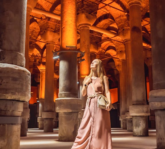 Visitor exploring the illuminated columns of the Basilica Cistern in Istanbul.
