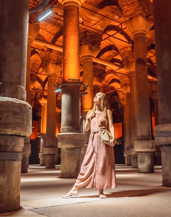 Visitor exploring the illuminated columns of the Basilica Cistern in Istanbul.