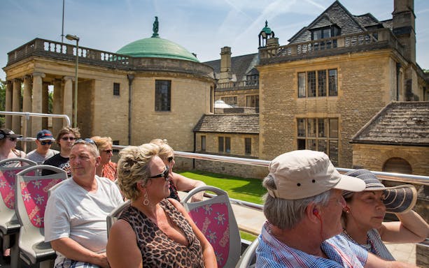 Tourists on an open-top bus during a 24/48-Hr Hop-On Hop-Off Tour of Oxford, passing historic buildings.